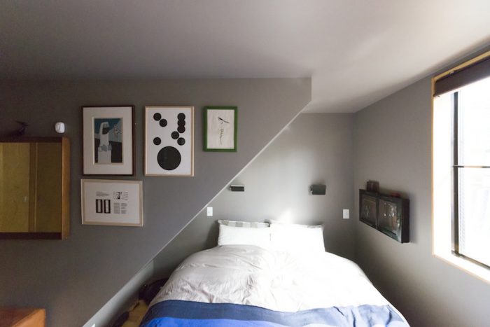 狭さが心地よい2階のベッドルーム。畦地梅太郎さんや小板橋雅之さんらの作品を壁に。ベッドヘッドの上にはシャルロット・ペリアンの照明を。