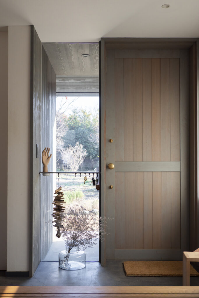 グレーに染色した米松を使用した玄関ドア。年月によって味わいが増す真鍮のドアノブとも好相性。横のFIX窓から風景が楽しめる。