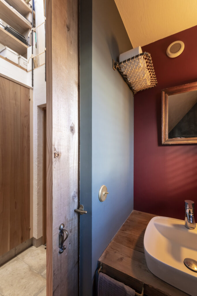 ２色使いの壁面がおしゃれなゲスト用トイレ。ロンドンの電車で使用していた吊り棚にトイレットペーパーを収納。屋内で扉があるのはここだけ。